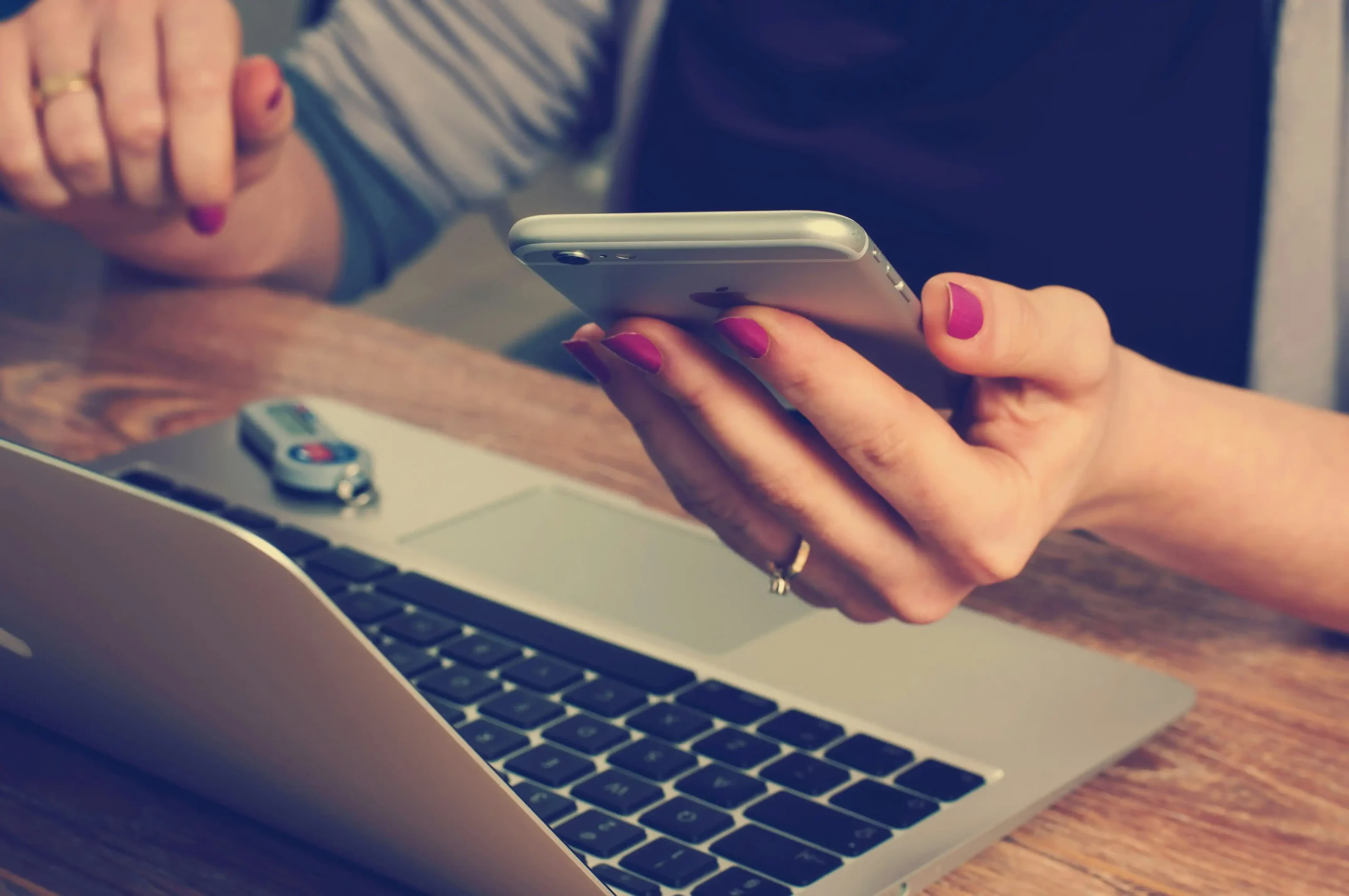 A woman holds a phone while looking at her computer
