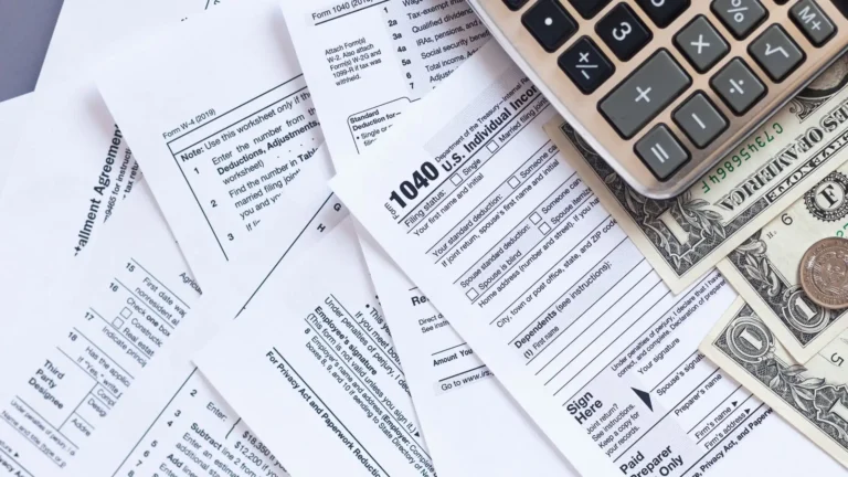 Various tax papers, money, and a calculator are spread out on the table in front of us in a flat lay.
