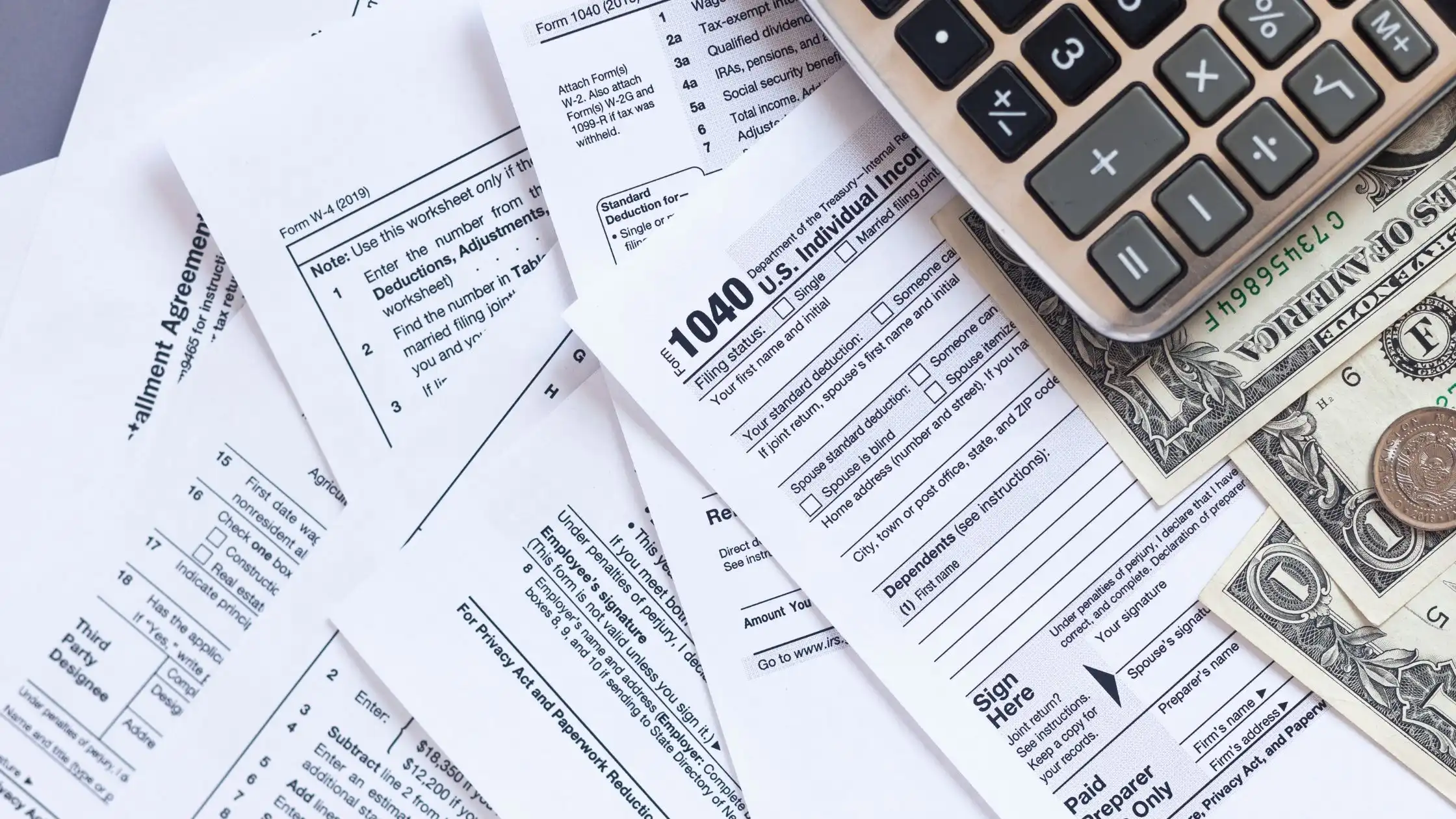 Various tax papers, money, and a calculator are spread out on the table in front of us in a flat lay.