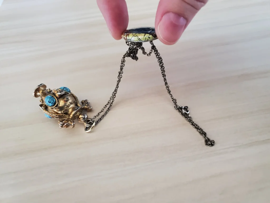 A magnet is held above a piece of jewelry, attracting the chain, indicating it is not pure gold