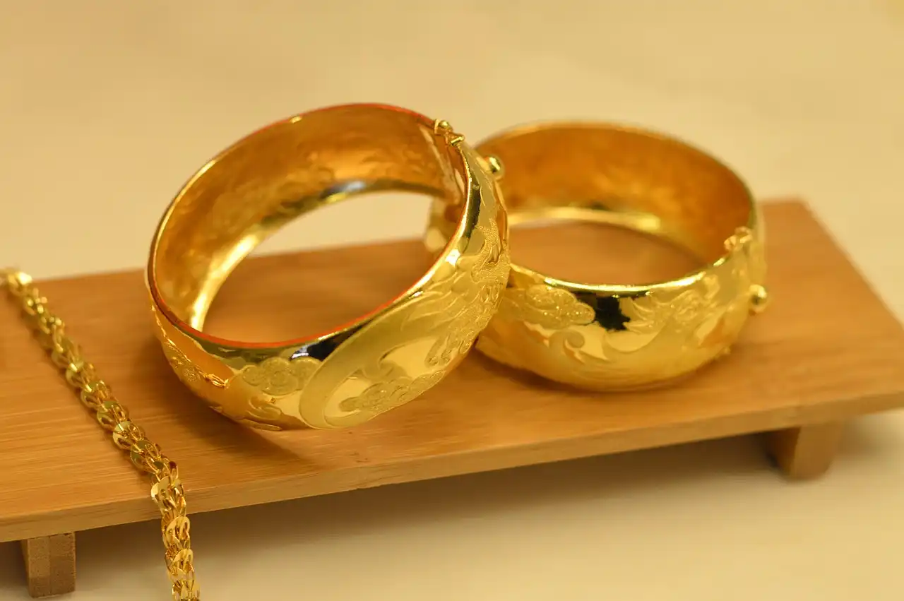 Two wide 24k wedding bangles sit atop a small wooden shelf.