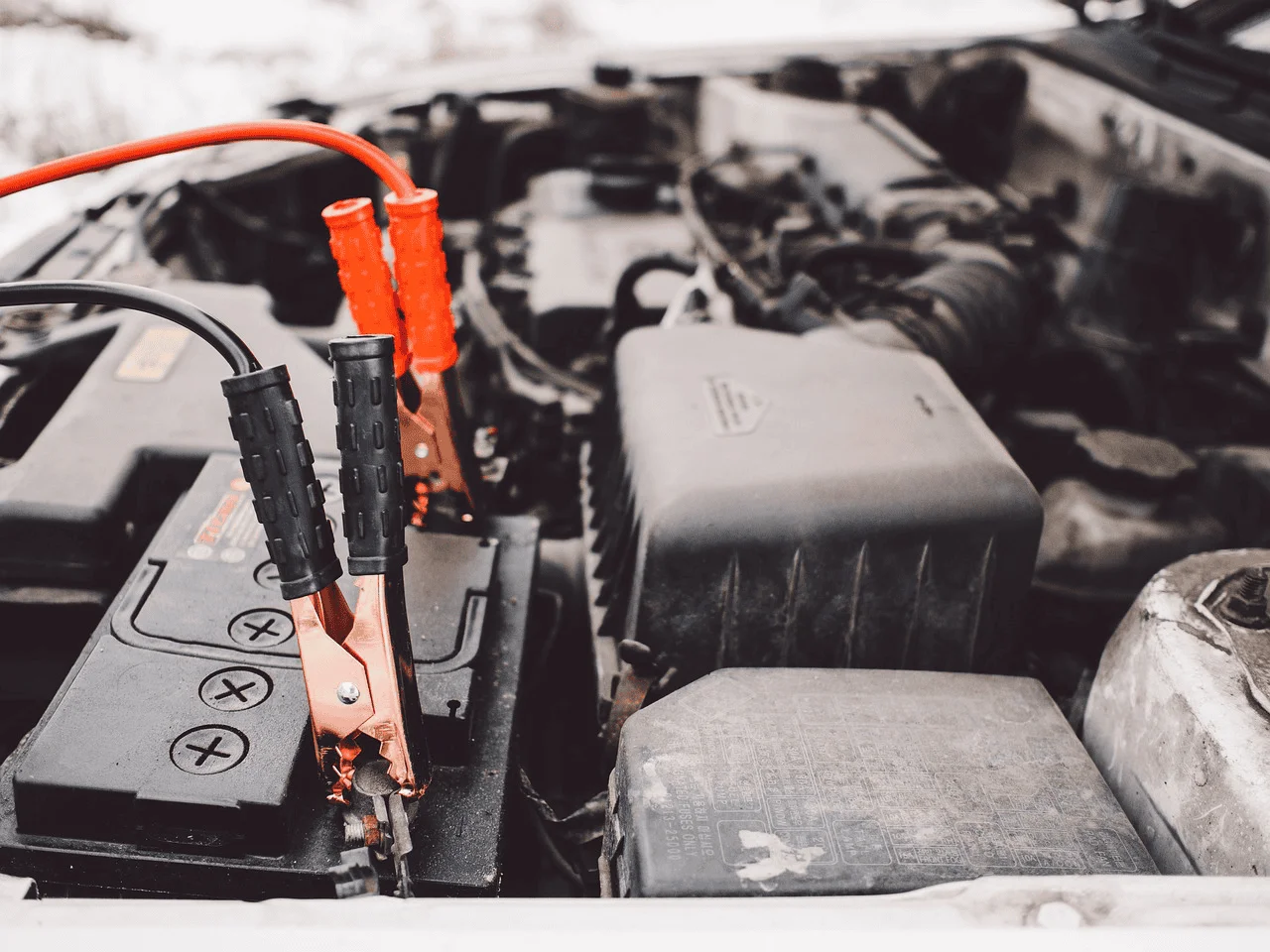 A set of jumper cables attach to a car battery under the hood.