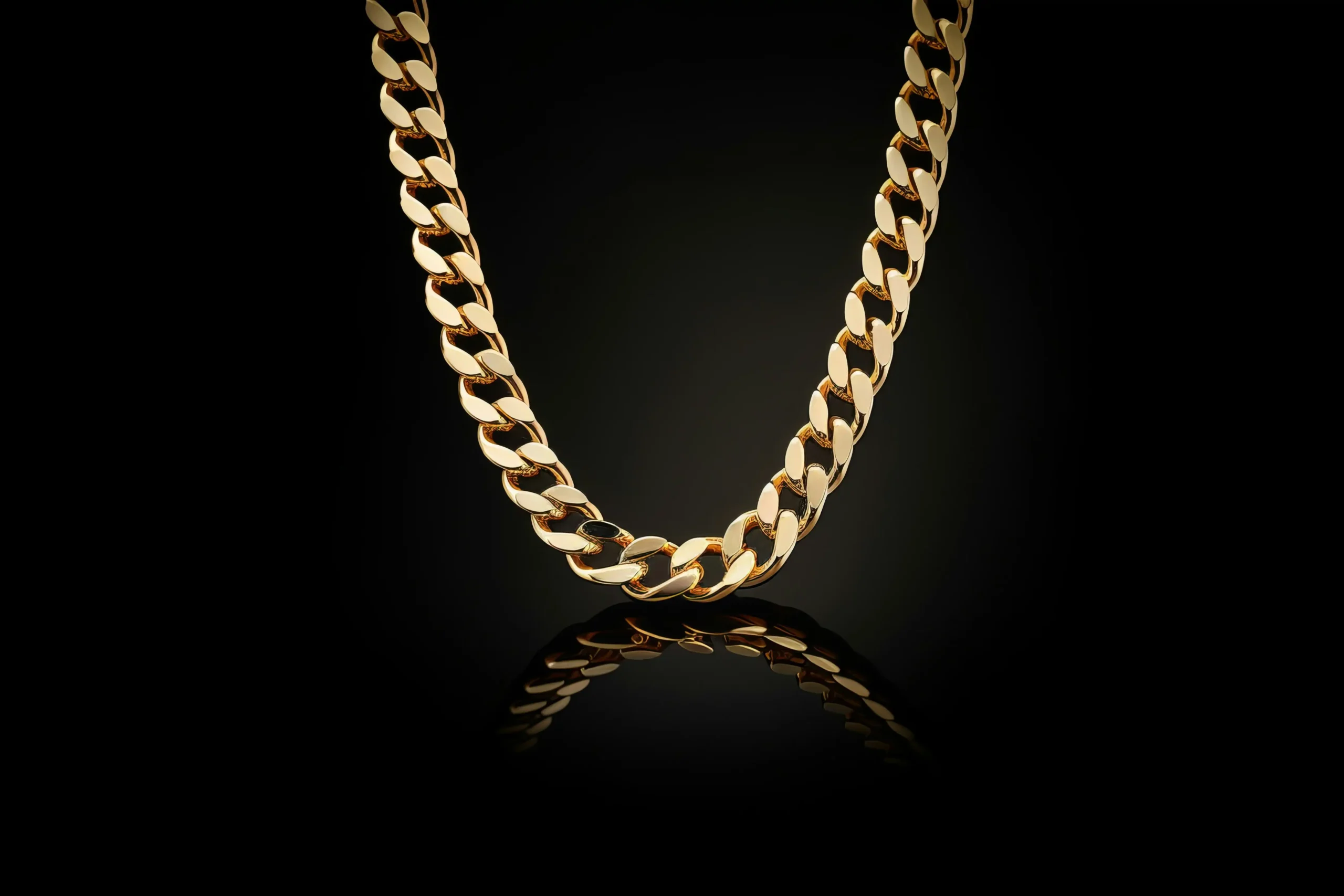 A thick gold chain dangles in front of a black backdrop and over a black reflective surface