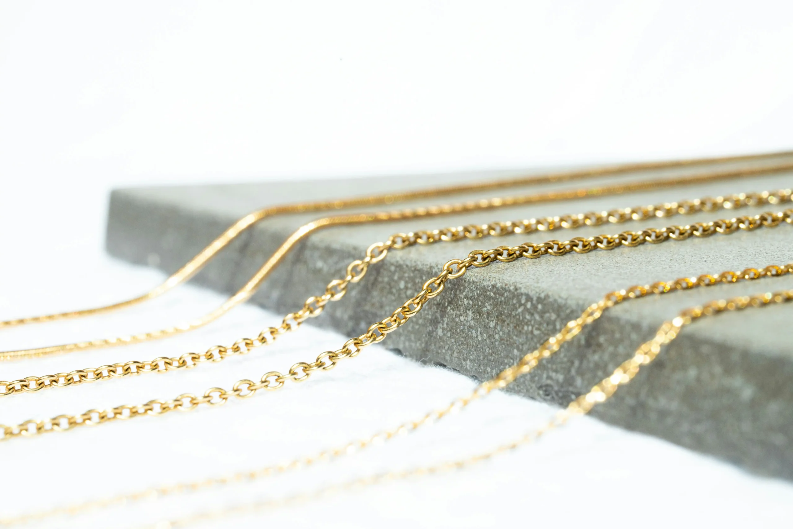 Three gold chains are draped across a cement block sitting on a white tabletop
