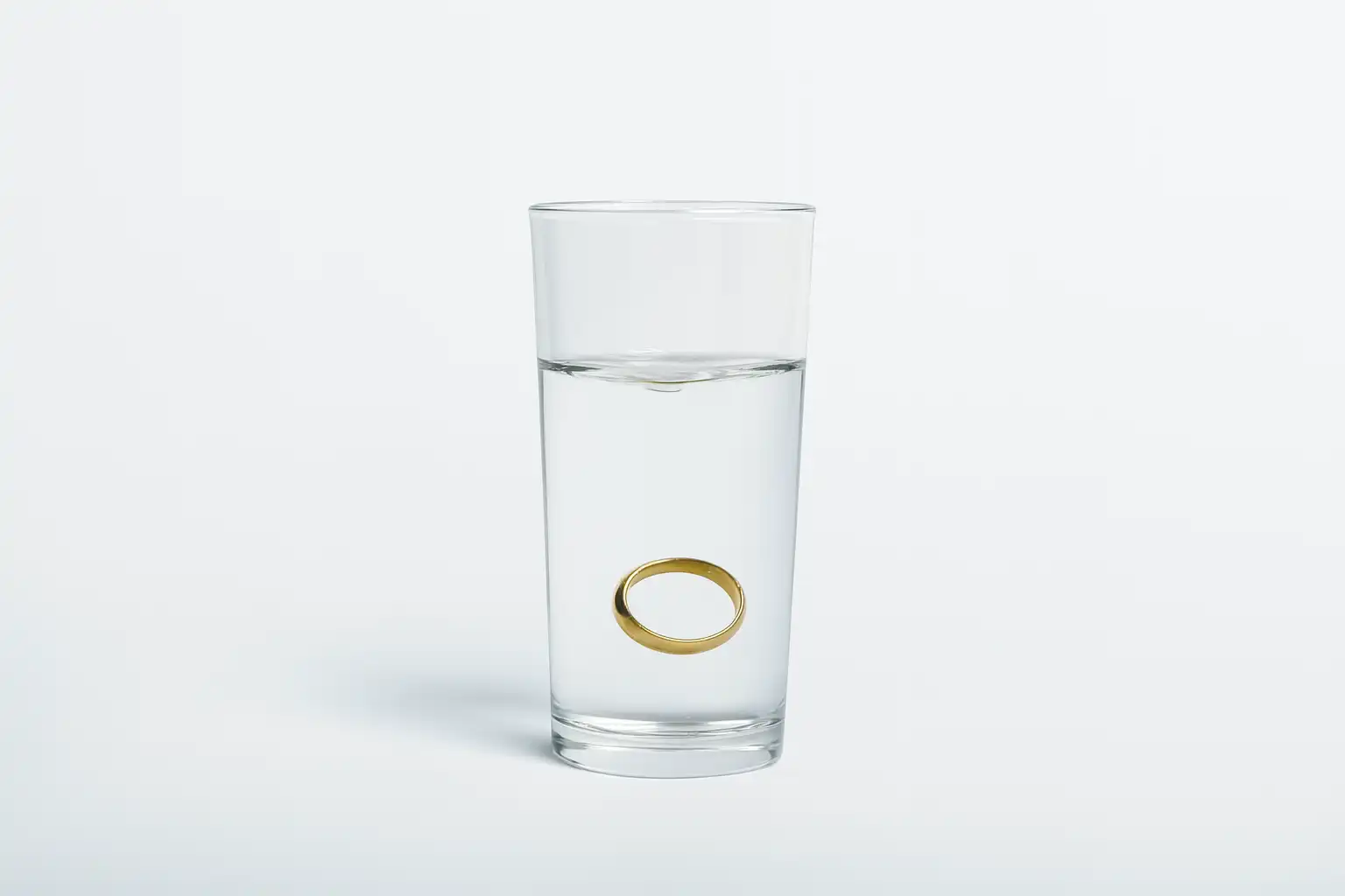 A gold band is dropped into a glass of water and is mid-sink to the bottom
