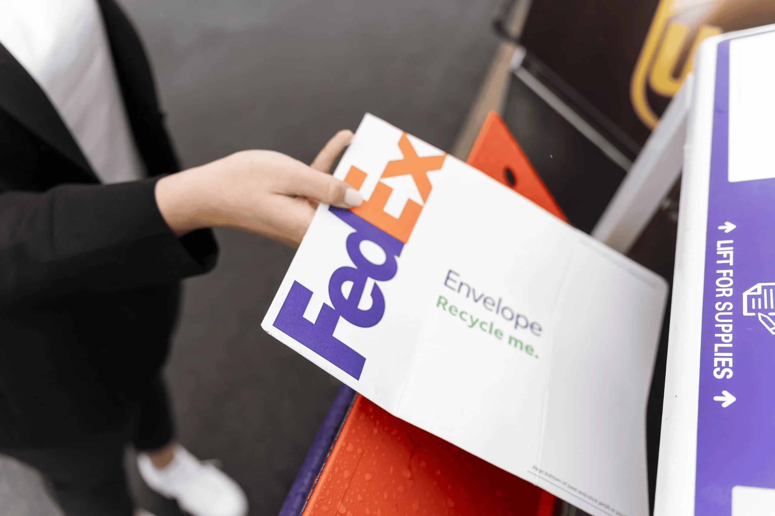 A FedEx envelope is being dropped into a shipping box by a woman