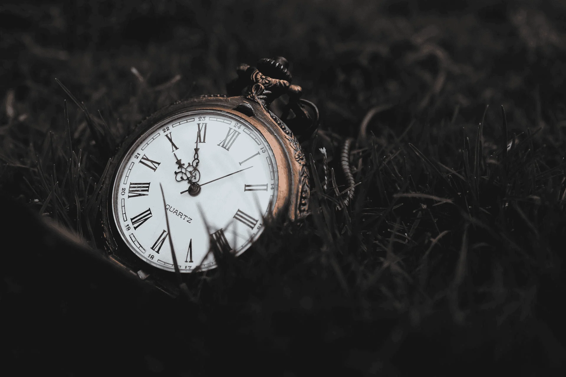 Pocket watch sits upon grass that has been turned black in post processing