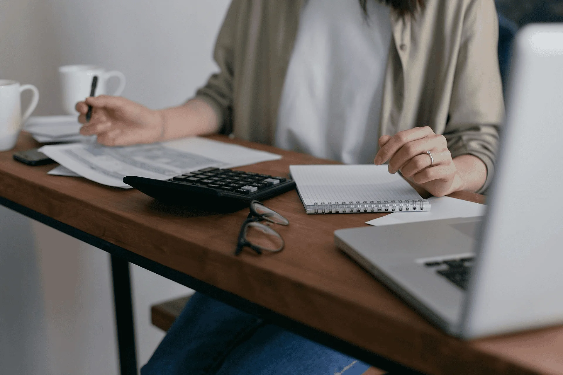 A woman sits by a computer with her calculator and figures her bills