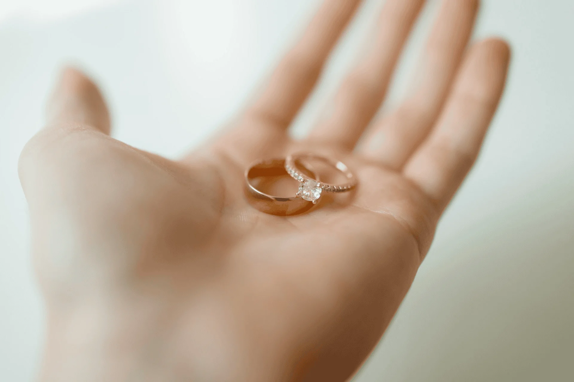 A woman's hand holds two gold wedding rings, a man's and a woman's